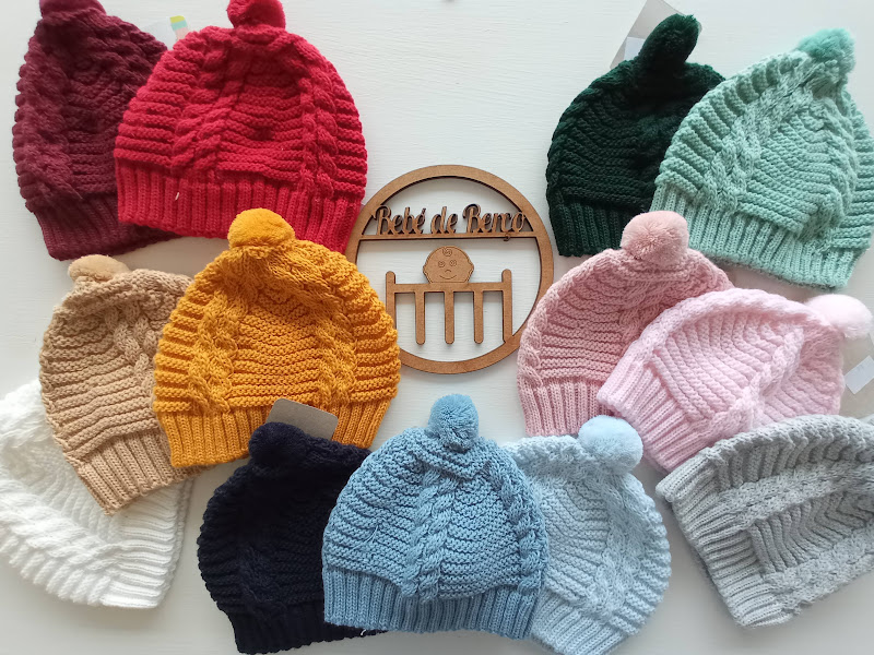 Vários gorros coloridos de malha com pom-pom em cima em redor de um símbolo decorativo de madeira