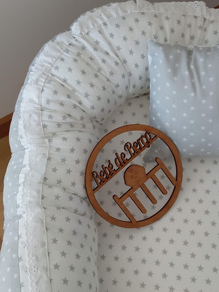 Berço com roupa de cama e almofada estampadas de estrelas cinza e enfeite de madeira com texto