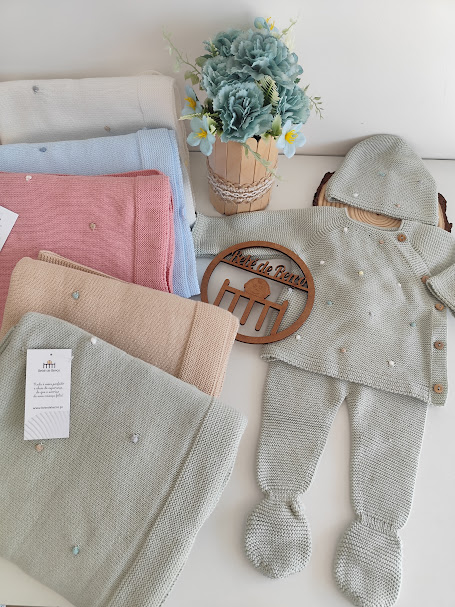 Conjunto de roupa de bebé tricotada com mantas coloridas e vaso de flores