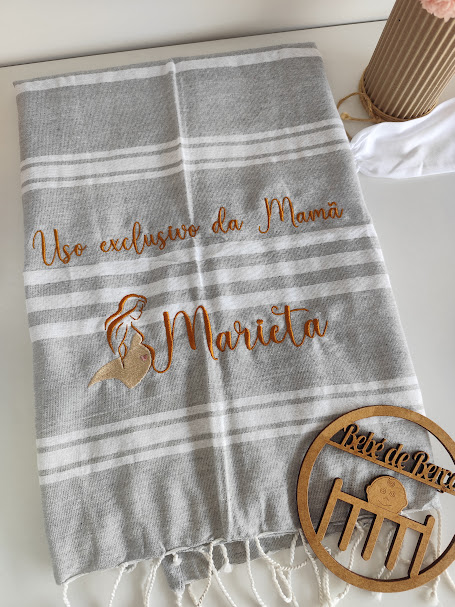 Toalha cinza com riscas brancas, bordado laranja com texto e imagem, máscara branca e decoração de madeira