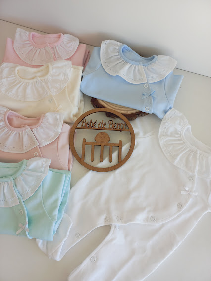 Conjunto de macacões de bebé com gola babado em várias cores claras e placa decorativa em madeira com texto