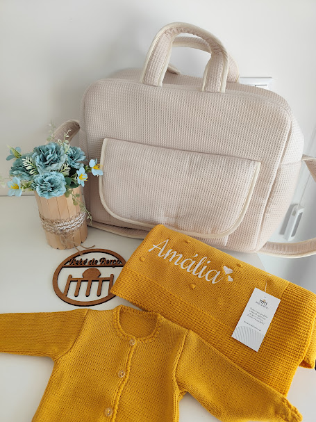 Bolsa bege tricotada, roupinha amarela de bebé, manta amarela com bordado Amália e vaso com flores azuis