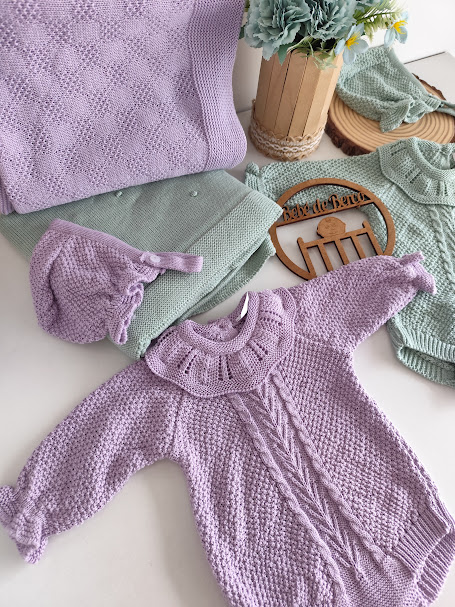 Roupa de bebé em malha lilás e verde-água com textura e folhos, decorada com flores e placa de madeira