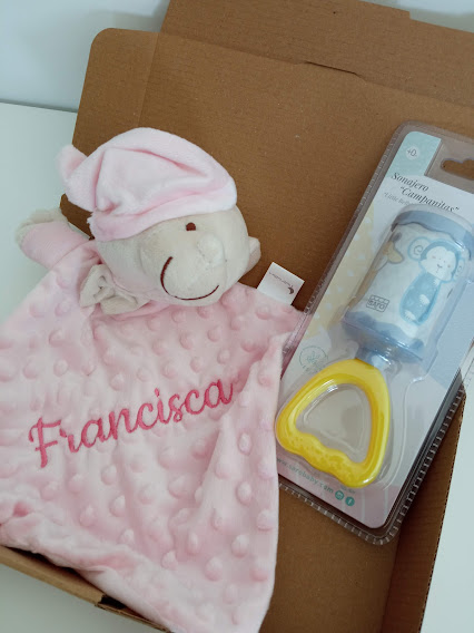 Brinquedo de pelúcia rosa bordado e chupeta em embalagem junto num fundo de cartão