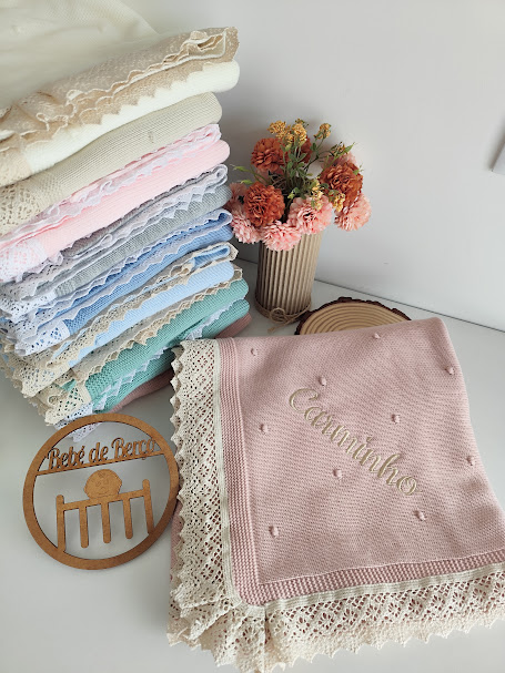 Mantas de bebé coloridas com bordas de renda e texto bordado, vaso com flores e placa de madeira