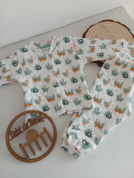 Pijama de bebé branco com padrão de animais e objeto redondo de madeira com inscrição