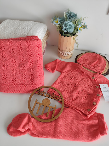 Conjunto de roupa de bebé coral, manta branca e creme, vaso com flores e placa decorativa de madeira