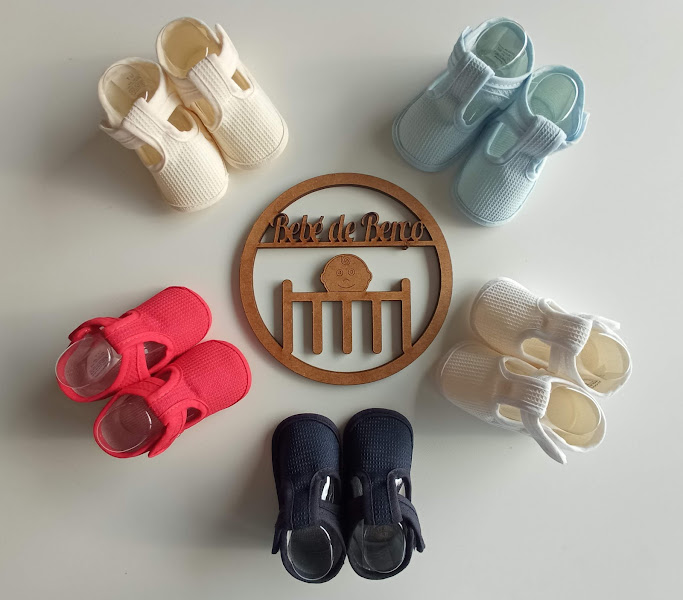 Cinco pares de sapatos tricotados para bebé em várias cores com placa de madeira no centro