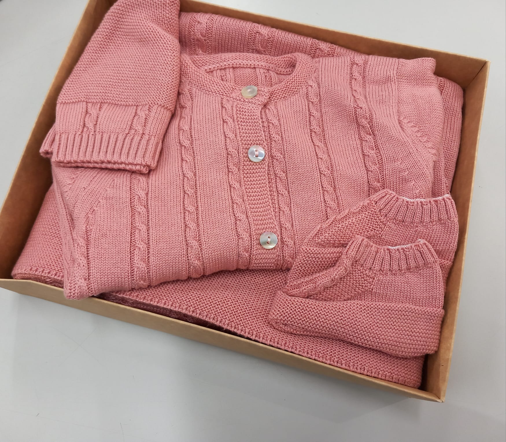 Conjunto de roupa de bebé cor-de-rosa em malha dentro de uma caixa castanha