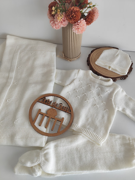 Conjunto de roupa de bebé em branco com camisola, calças, touca e manta com padrão de ponto trabalhado.