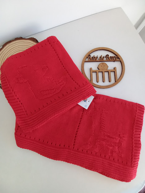 Cachecol vermelho de malha com padrão de animal em relevo e objeto de madeira com texto Pérolas de Banho