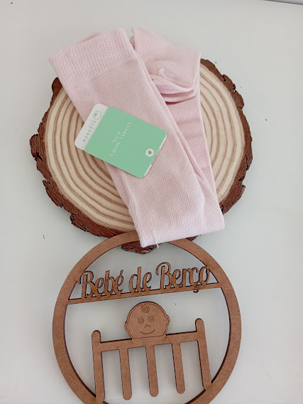 Meias cor-de-rosa com etiqueta sobre pedaço de madeira e placa de madeira 'Bebé de Berço'.
