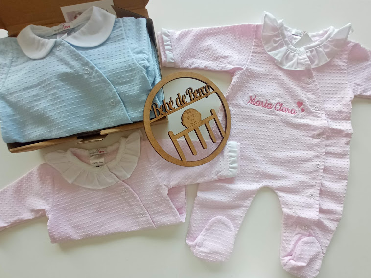 Roupas de bebé em algodão texturizado azul e cor-de-rosa com golas de babados e objeto de madeira decorativo