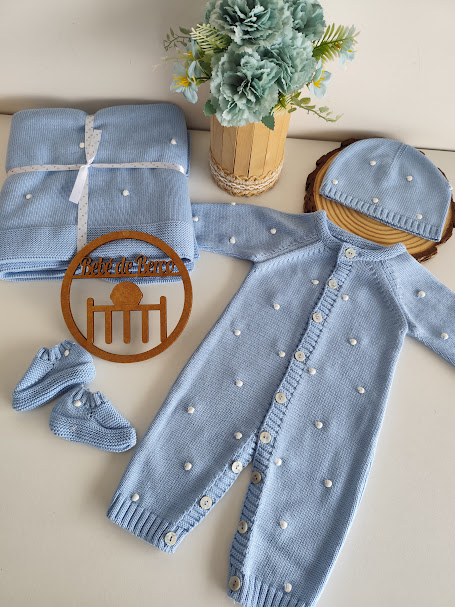 Conjunto de roupa de bebé azul claro em malha com detalhes brancos em ambiente neutro.