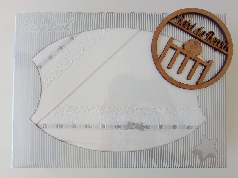 Toalha de bebé branca com renda e laço, em caixa branca com riscas e estrela, e placa de madeira com nome