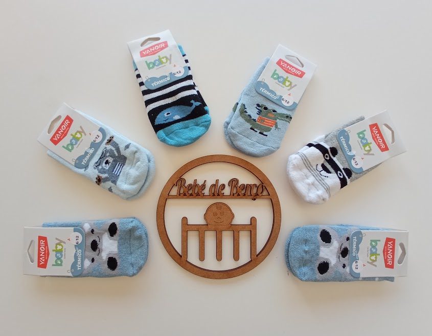 Seis pares de meias para bebé com padrões de animais e riscas, etiquetadas, dispostas em círculo em volta de um emblema de madeira com texto e figura.