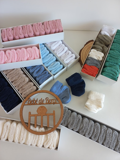 Várias caixas abertas com meias multicoloridas para bebé e convite decorativo em madeira