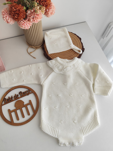 Babygrow branco de malha com padrão de bolinhas e capuz, com decoração floral em vaso e suporte de madeira redondo com texto
