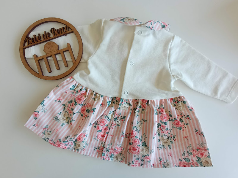 Veste de bebé branca com saia floral cor-de-rosa e verde e placa de madeira decorativa redonda