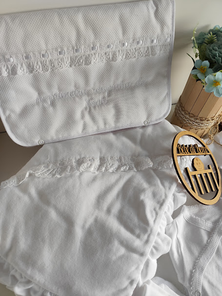 Artigos têxteis brancos com bordados e renda, arranjo floral em vaso de madeira