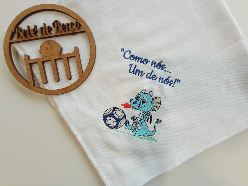 Pano de cozinha branco com dragão azul e frase, junto a objeto redondo de madeira com texto