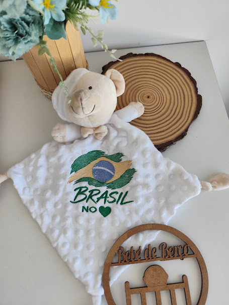 Cobertor de pelúcia branco com ursinho e bordado da bandeira do Brasil.