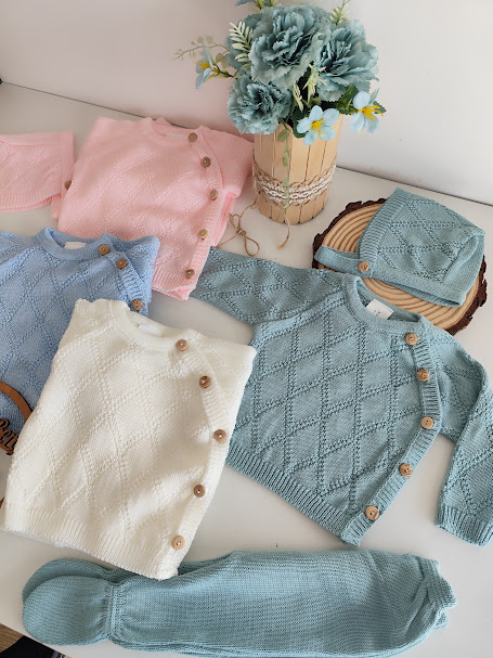 Conjunto de roupa de bebé em malha com botões de madeira e vaso com flores artificiais