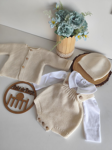 Conjunto de roupa de bebé bege e branco com arranjo floral e base de madeira