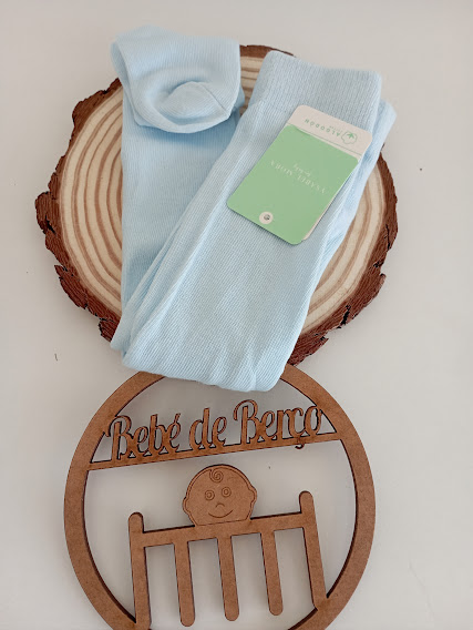 Par de meias azuis claras com etiqueta, sobre tábua redonda de madeira e decoração com texto Bebé de Berço