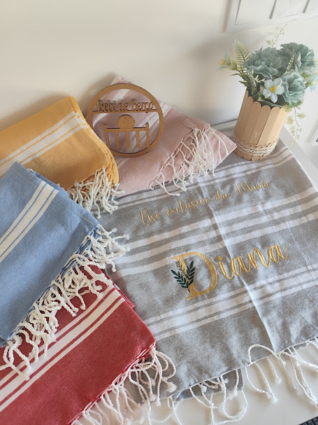 Lenços coloridos com franjas e lenço cinzento bordado com nome Diana com decoração de planta e sinal de madeira.