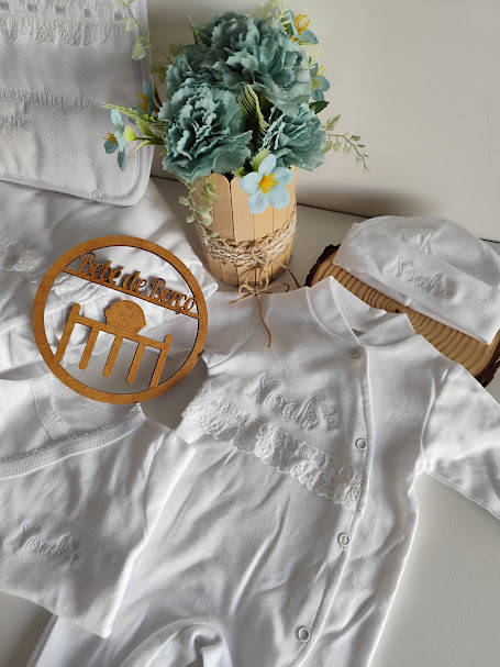 Roupas de bebé brancas com bordados e flores artificiais num vaso decorativo