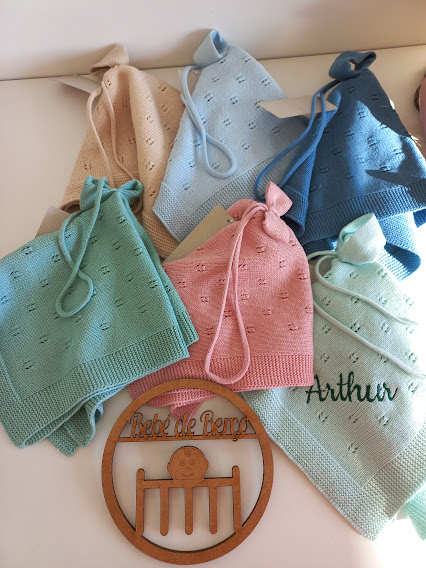 Toucas de malha coloridas em tons pastel com placa decorativa de madeira.