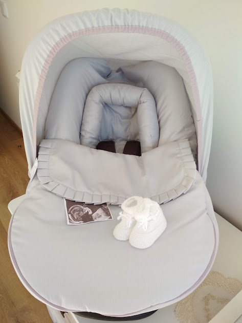 Carrinho de bebé cinzento claro com capota branca e sapatinhos brancos