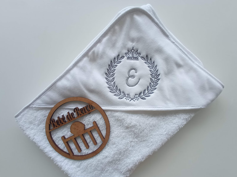 Toalha branca com bordado cinza e objeto redondo de madeira