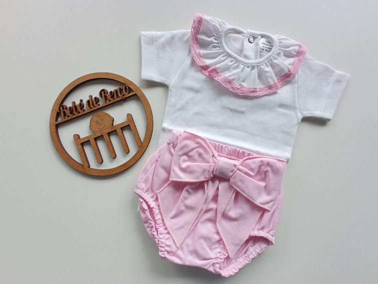 Conjunto de bebé branco e rosa com folho e laço, sobre fundo branco