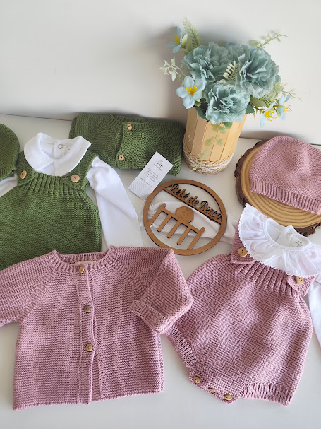 Roupas de bebé em malha verde e rosa com botões, com flores artificiais num vaso