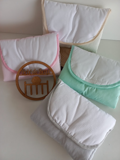 Quatro fraldas/bolsas em tecido com bordas coloridas e círculo de madeira com texto Bebé de Bambu