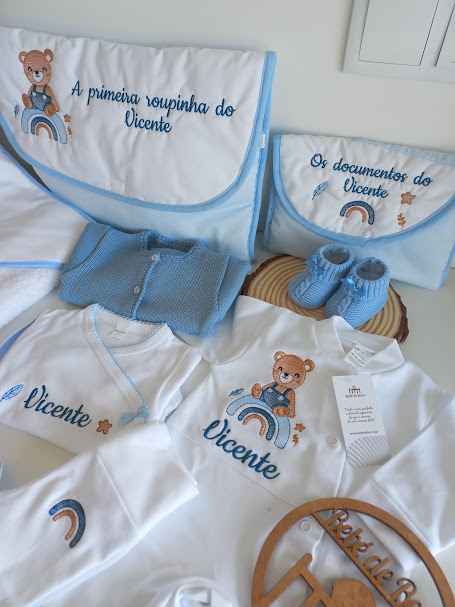 Conjunto de roupa de bebé azul e branca com bordados personalizados e acessórios organizadores.