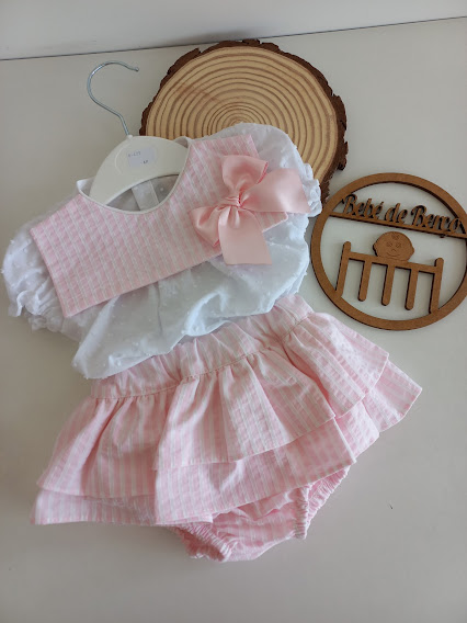 Conjunto infantil branco e rosa com saia e laço, em fundo claro e objeto de madeira