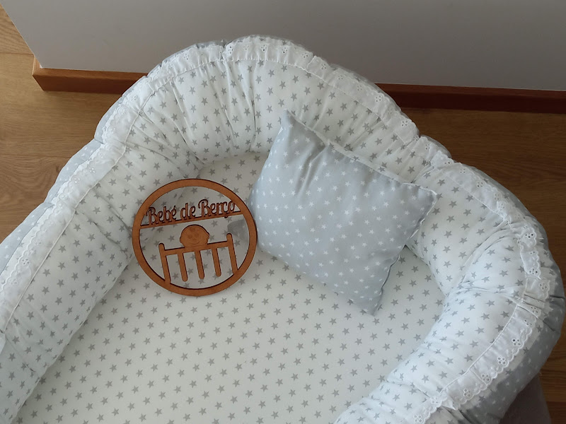 Mini berço redondo acolchoado branco com almofada cinzenta e placa de madeira com texto