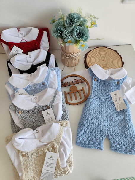 Conjuntos de roupa para bebé em várias cores com camisa branca e jardineira de malha, arranjo de flores azuis