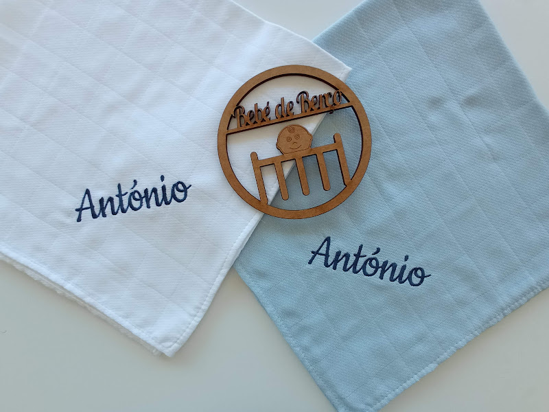 Dois panos de tecido com nome António bordado e um círculo de madeira com texto gravado