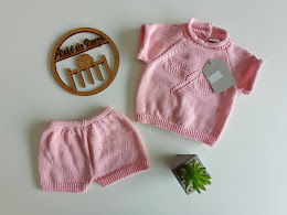 Conjunto de roupa de bebé cor-de-rosa em malha tricotada com etiqueta, círculo de madeira e planta em fundo branco