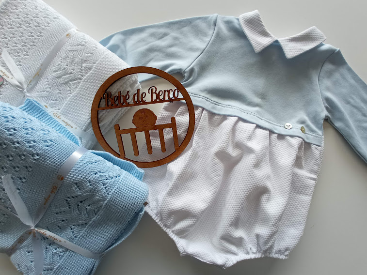 Roupa de bebé azul celeste e branca com cobertores e círculo de madeira com texto Pé de Berço