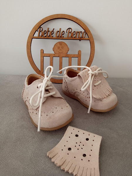 Sapatos de bebé em camurça bege com atacadores brancos e placa decorativa de madeira com texto 