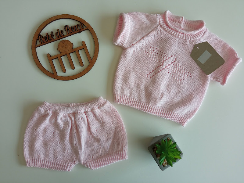 Conjunto de roupa de bebé cor-de-rosa clara com camisola e calções em malha, disco de madeira com texto gravado e planta pequena