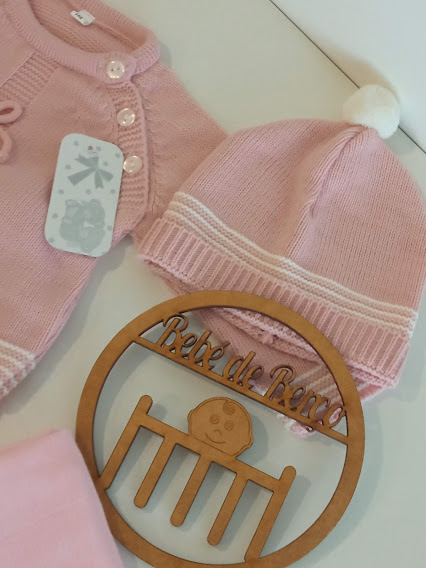 Conjunto de roupa de bebé rosa com casaco, gorro e objecto decorativo de madeira.
