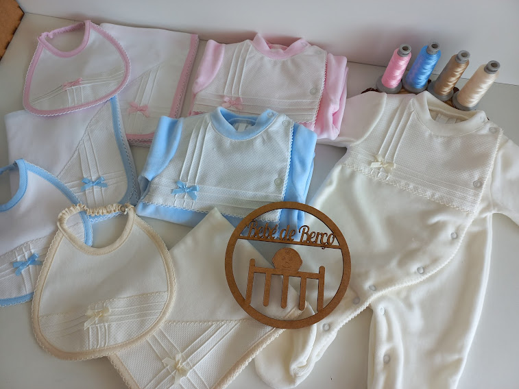 Produtos de bebé em tecido branco, azul, rosa e bege com rendas e laços