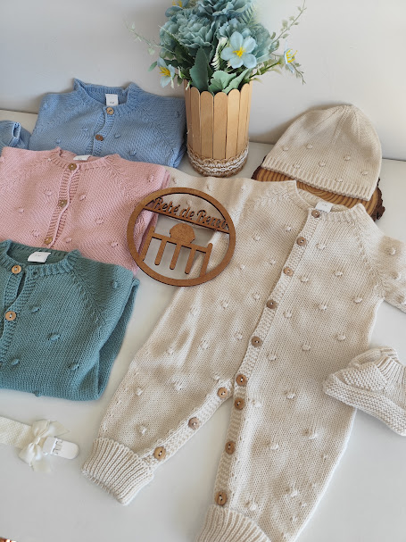 Roupas de bebé coloridas em malha com textura decorativa, vaso com flores e placa decorativa em madeira