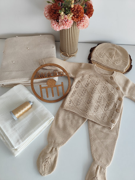 Conjunto de roupa de bebé bege em malha com padrão, mantas e vaso com flores